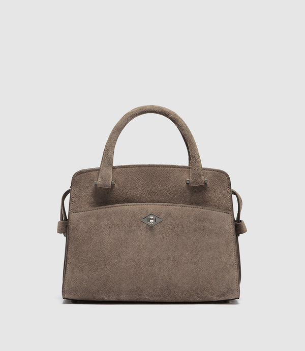 A taupe brown suede handbag with dual top handles, a front slip pocket, and a small silver-tone diamond-shaped logo clasp, shown against a light gray background.