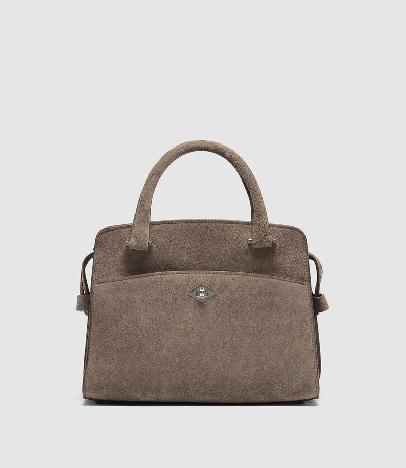 A taupe brown suede handbag with dual top handles, a front slip pocket, and a small silver-tone diamond-shaped logo clasp, shown against a light gray background.